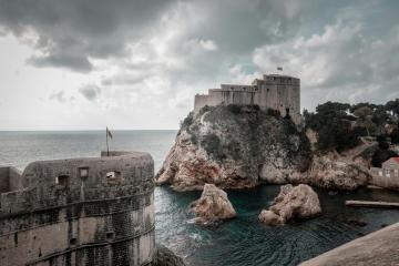 Majestic view of Dubrovnik's medieval forts and rocky coast under dramatic skies.