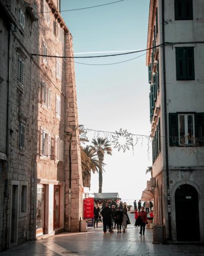 A bustling pedestrian walkway in Split, Croatia, featuring historic stone buildings and palm trees under a clear sky.