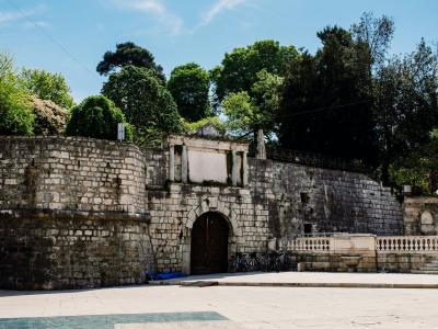 Explore the ancient stone gateway in Queen Jelena Madijevka Park, Zadar, with vibrant greenery and clear skies.