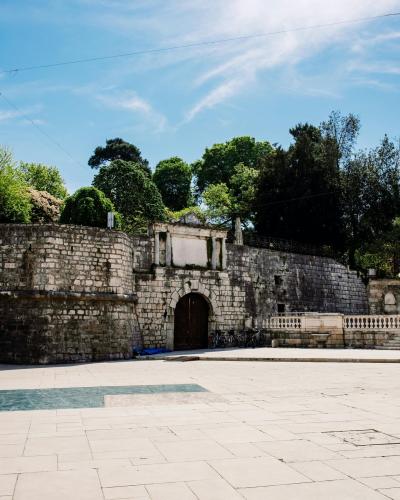 Explore the ancient stone gateway in Queen Jelena Madijevka Park, Zadar, with vibrant greenery and clear skies.