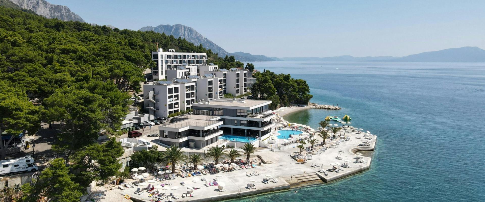 Scenic aerial photograph of a beachside resort in Podaca, Croatia surrounded by turquoise sea and lush greenery.